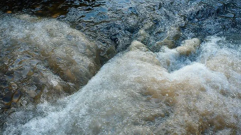A photorealistic image of two streams of water, one clear and one murky, starting to mix uncontrollably in a turbulent confluence. The image represents the danger of commingling funds, with dramatic cinematic lighting emphasizing the chaos and loss of distinction, 8K, sharp focus, depth of field, shot on a high-end DSLR.